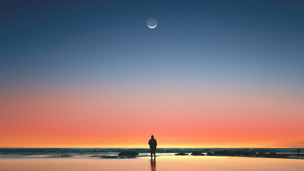 man on beach looking at new moon